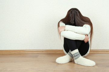 Sad woman sitting on floor near wall