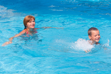 Mother train her son to swim in the pool.