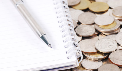 silver pen on notebook with coins background