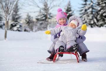 children dressed in warm clothes near forest sit on sled