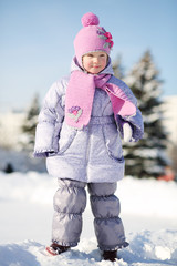 Smiling little girl dressed in pink scarf and hat stands