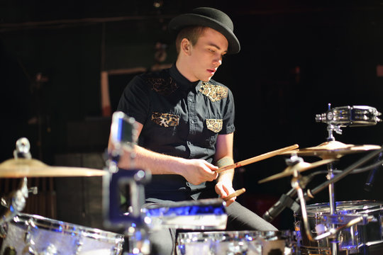 man in hat plays drum set in night club.