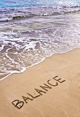 Word BALANCE written on sand, with sea waves in background