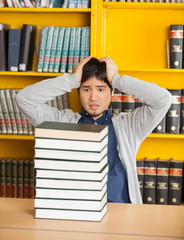 Confused Man Looking At Stacked Books In Library