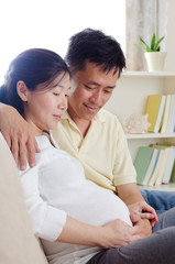 Asian man and pregnant wife sitting on sofa