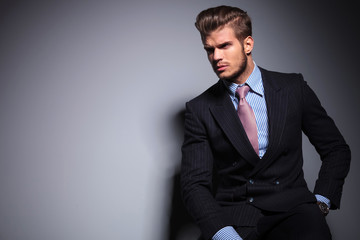 seated young fashion model in suit looks away