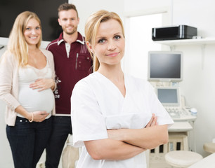 Confident Gynecologist With Expectant Couple In Background