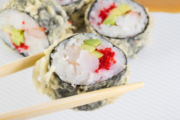 Sushi roll in tempura on white plate and chopsticks