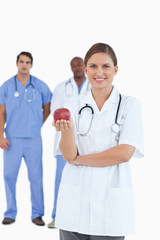 Fototapeta premium Smiling doctor with apple and colleagues behind her