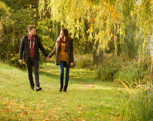 Naklejka na ściany i meble man and woman holding hands walking in the autumn park