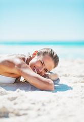 Portrait of smiling woman in swimsuit laying on sandy beach