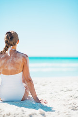 Young woman in swimsuit sitting on beach . rear view