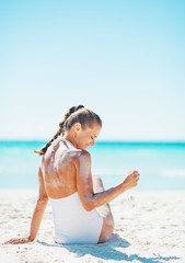 Woman in swimsuit sitting on beach and playing with sand