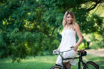 Fototapeta na wymiar Beautiful young woman portrait with bicycle in a park.