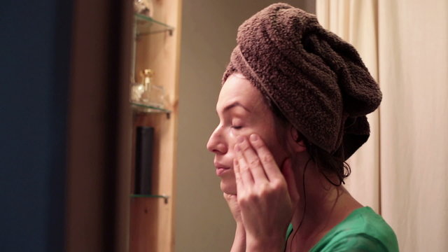 Attractive woman applying moisturiser creme on her face in bathr