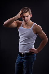 Sexy young man wearing white undershirt and jeans, posing over d