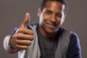 smiling dark-skinned young man showing thumbs up and winks