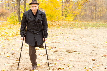 One-legged man walking with crutches in the park