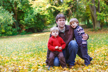 Happy father with two little sons having fun in autumn park.