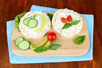 Tasty crispbreads with vegetables on wooden background