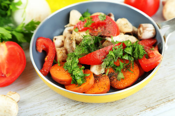 Sliced fresh vegetables in pan on wooden board isolated on