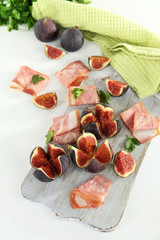 Tasty figs with ham on white wooden table