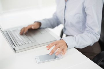 Side view mid section of a businesswoman using laptop and cellph