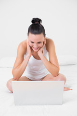 Casual smiling woman looking at laptop in bed