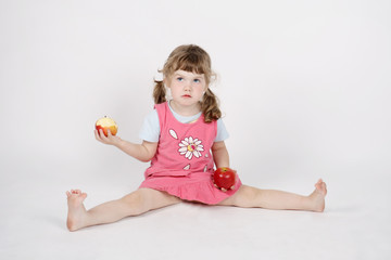 Obraz na płótnie Canvas Little beautiful girl eats apple and holds second apple on floor