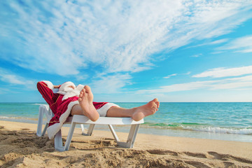 sunbathing Santa Claus relaxing in bedstone on tropical sandy be