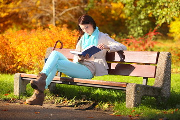 Obraz premium Young girl relaxing in autumnal park reading book