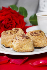 Cinnamon rolls on white plate among rose petals