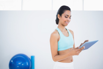 Fototapeta na wymiar Pretty sporty woman standing in fitness hall using her tablet
