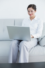 Smiling well dressed woman using laptop on sofa