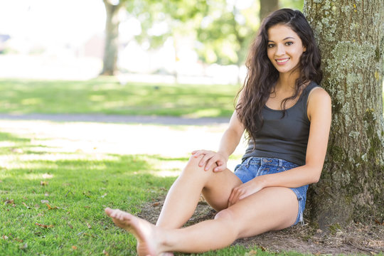 Casual attractive brunette sitting leaning against tree