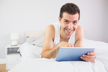 Smiling handsome man lying in bed using tablet