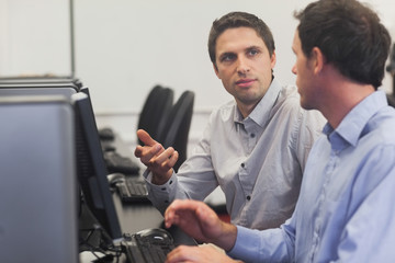 Two handsome men talking while sitting in computer class
