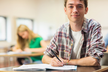 Smiling student with others writing notes in classroom