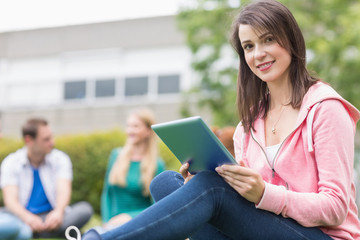 Fototapeta premium Smiling college girl using tablet PC with students in park