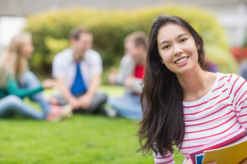 Fototapeta na wymiar Smiling college student with blurred friends in the park
