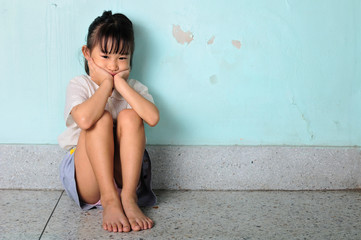 sad and depressed little girl sitting near the wall
