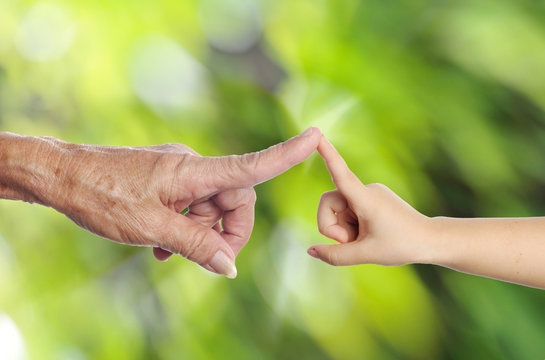 Senior's hand touching a child's hand on green nature background