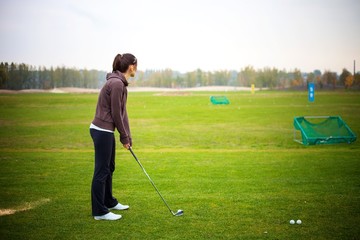 Obraz premium Young woman training golf at the driving range