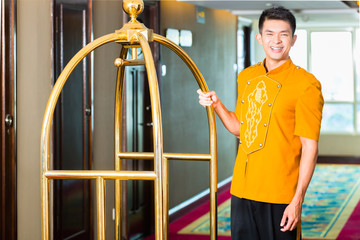 Asian bell boy or porter bringing suitcase to hotel room