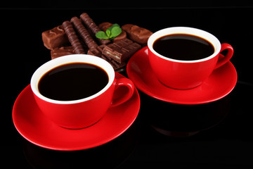 Red cups of strong coffee and chocolate bars isolated on black