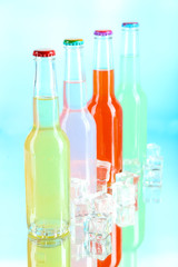 Drinks in glass bottles with ice cubes on blue background