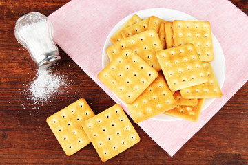 Delicious crackers with salt and napkin on wooden background