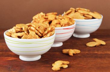 Delicious crackers in bowls on wooden table on brown background