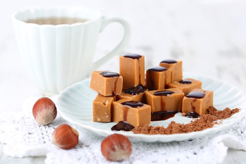 Many toffee on plate and cup of tea on napkin on wooden table