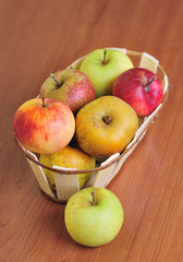 basket with several kinds of apples on a wooden table